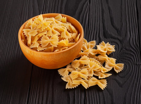 Uncooked farfalle rigate pasta in wooden bowl on black wooden backgroundの写真素材