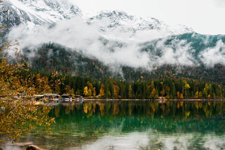 Cozy autumn morning in the Bavarian mountains, Germany. Alps landscape with lake coast, small village, clouds, forest and reflection in waterの写真素材