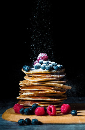 Stack of pancakes with blueberry, raspberries and honey on the wooden cutting board. Breakfast, food...