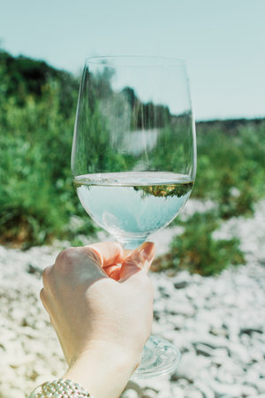 Hand with white wine glass on summer nature green background. Sea beach. Vacation and restの写真素材