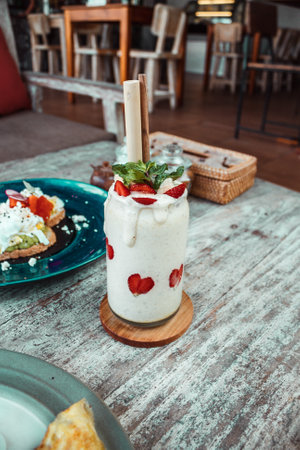 White smoothie in glass with straw, sliced strawberry on wooden table. Healthy dessert for breakfastの写真素材