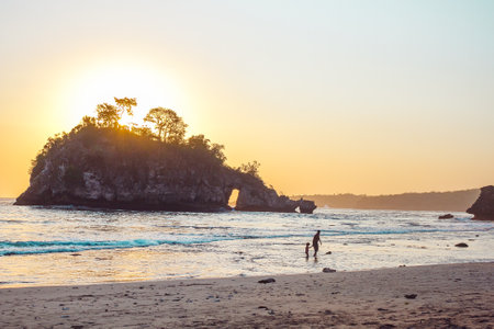 Father and child on the beach. Sunset the ocean. A little island near a cost. Cliffs and wavesの写真素材