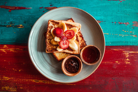 French toast with strawberries, banana, top view. Plate of sweet food on wooden colorful backgroundの写真素材