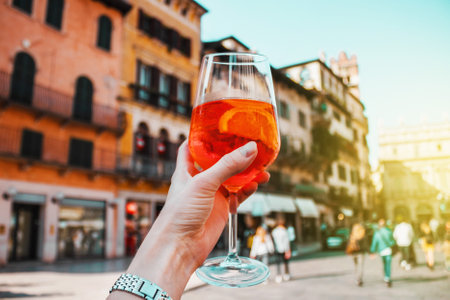 Female hand with glass of orange cocktail spritz near old buildings. Sunny day in Verona, Italyの写真素材
