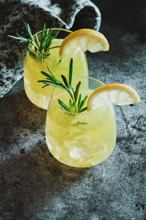 Cold cocktail, lemonade with lemon sliced, rosemary plant on dark concrete background. Drink photo