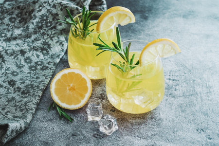 Cold cocktail, lemonade with lemon sliced, rosemary plant on dark concrete background. Drink photoの写真素材