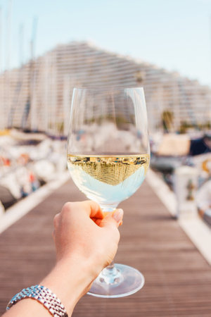 Woman hand with white wine, champagne glass on yachts, sailing boats background. Nice, France.の写真素材