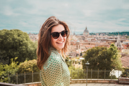 Profile portrait of young smiling woman in sunglasses with a panoramic view of Rome. Girl traveler on vacation in Italy. Sunny day in southern Europe.の写真素材