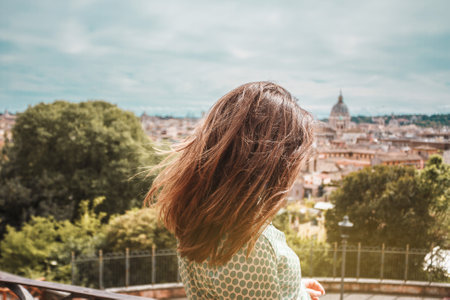 Young brown hair woman with her back on a background of Rome panoramic view. Girl traveler on vacation in Italy. Sunny day in southern Europe.の写真素材