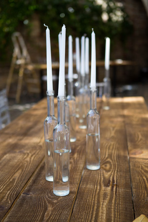 White candles in bottles of wine stand on white table