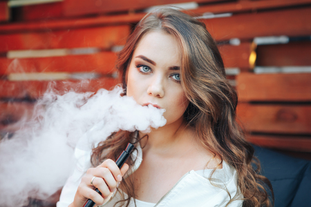 Young woman smoking a hookah outdoors. The pleasure of smoking. Portrait of a smoking young woman. Background a wooden wall.の写真素材