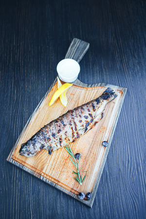 Grilled fish on a cutting wooden board. wooden background.の写真素材