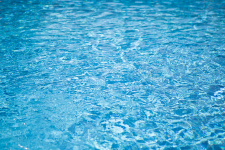 Ripple water in swimming pool with sun reflection. Blue water abstract background.