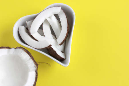 Half and slices of coconut, heart shaped plate, on yellow background with copy space, top view, flat lay.の写真素材