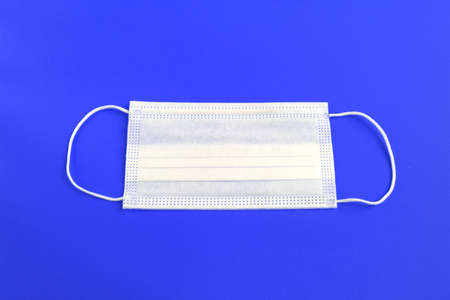 White medical protective mask isolated on blue background.の写真素材
