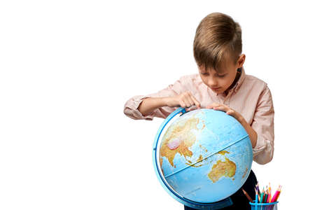 European schoolboy carefully looks at the globe and looks for the city of America in geography lessonの写真素材