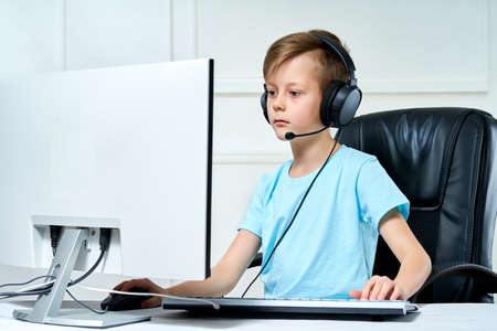 Child in headphones looks at a personal computer monitor, streams plays a computer game, broadcasts...
