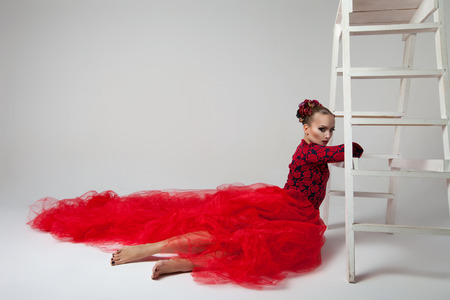 beautiful woman in red dress sitting near the white stairsの写真素材
