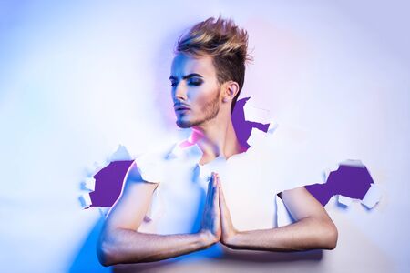 beautiful transvestite with a female make-up breaks through a paper background