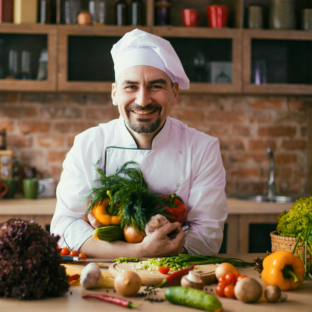 young chef in the kitchen, on the table fresh vegetables for cookingの写真素材
