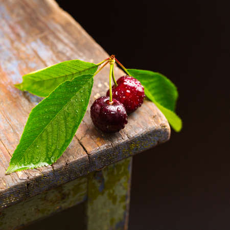 two berries lie on a wooden table, red cherries with leavesの写真素材