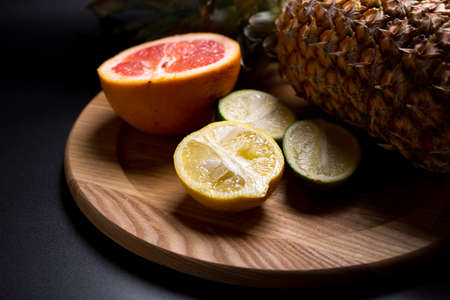 lemon, lime, grapefruit with pineapple lie on a wooden tray, fruits on a dark backgroundの写真素材