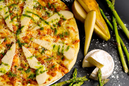pizza with pear, cheese and asparagus. appetizing and juicy pizza on a dark backgroundの写真素材