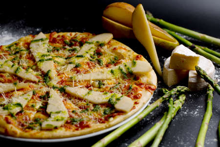 pizza with pear, cheese and asparagus. appetizing and juicy pizza on a dark backgroundの写真素材