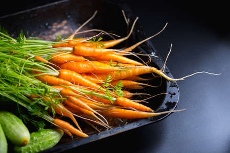 young carrots with cucumbers on a dark background, fresh vegetables from the gardenの写真素材