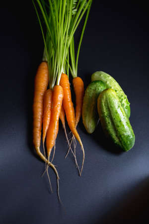 young carrots with cucumbers on a dark background, fresh vegetables from the gardenの写真素材