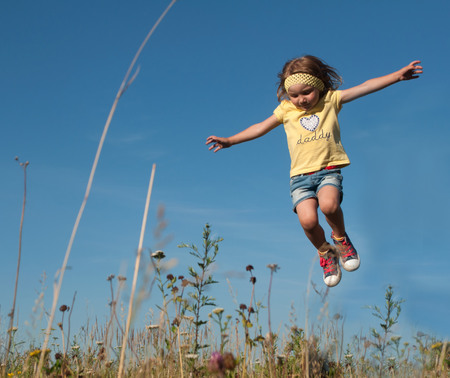 A little girl jumping against the blue sky backgroundの写真素材