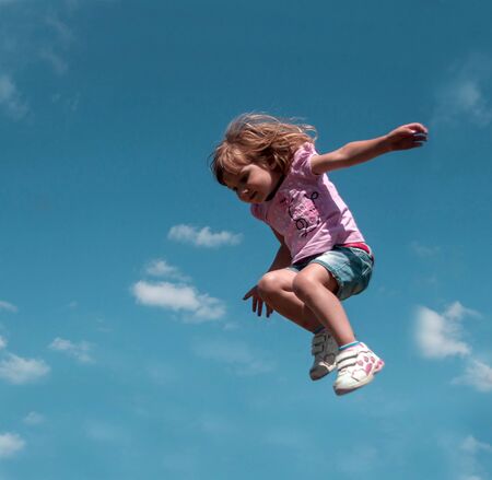 A little girl jumping against the blue sky backgroundの写真素材