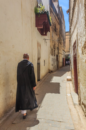 Fes, Morocco - May 11, 2013: Man in djellaba, berber clothing walking down a narrow street in Fes Medina in Morocco3: Man in djellaba, berber clothing walking down a narrow street in Fes Medina in Moroccoのeditorial素材