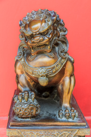 Bronze Chinese lion sculpture male of the pair holding a ball representing the world in his front paw symbol of protection and power in Asiaの写真素材