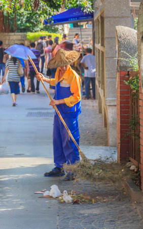 September 14, 2013 -Gulangyu, China: Street sweeper sweeps a busy shopping street in center of the islandのeditorial素材