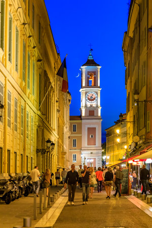Nice, France - May 27, 2017: People walking in the streets of the Old Town, fille with restaurants and cafes. Clock Tower and a sliver of the new moon in the backgroundのeditorial素材