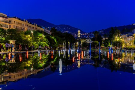 Nice, France - May 25, 2018: Reflecting fountain on Promenade du Paillon, surrounded by a green urban park, lit up with red and blue lights at sunset at Place Massena or Massena squareのeditorial素材