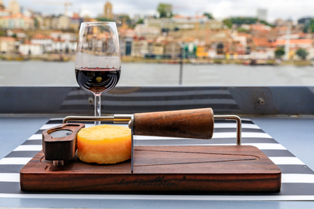 Glasses of port wine and a small wheel of cheese on the board at an outdoor restaurant with the Douro river and Dom Luis I bridge blurred in the background in Porto, Portugalの写真素材