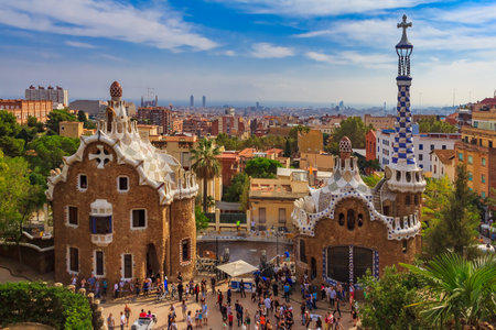Two buildings at the entrance of the famous Antoni Gaudi Park Guell in Barcelona, Spain with the view of the city skyline in the backgroundのeditorial素材