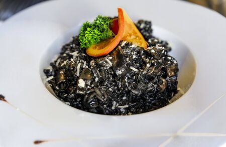 Squid ink black risotto with squid rings sprinkled with parmesan, served with a slice of orange and parsley at a high end restaurant in Montenegroの写真素材