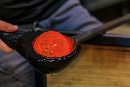 Glass blower shaping a bubble of melted glass on a rod by hand in the manufacturing process at a glass maker's workshop, shallow depth of fieldの写真素材