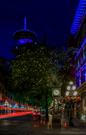 Vancouver, Canada - July 09, 2019: Traffic light trails after sunset by the steam clock in Gastown with the Vancouver Lookout tower in the backgroundのeditorial素材