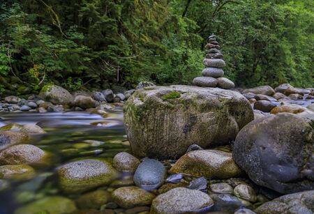 Rock pile or cairn in the clear water stream, silky long exposure motion, with pine forest in the background in Lynn Canyon Park, Vancouver, Canadaの写真素材