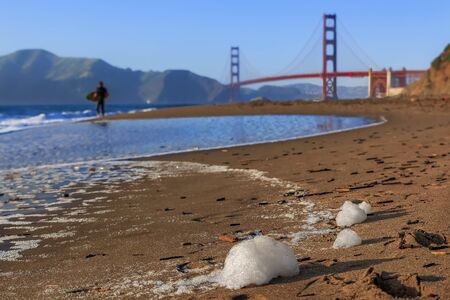 Blurred view of an unidentified surfer at sunset at Baker Beach by the famous Golden Gate Bridge in San Francisco California, United States of Americaの写真素材