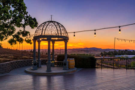 Outdoor al fresco chairs and table on a wooden deck at sunset in the spring with grape vines and hills in the background, Napa Valley, California USAの写真素材
