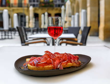 Glass of Spanish rose or rosado wine and Jamon Iberico tostada or ham and tomato sandwich at an outdoor restaurant in Pamplona, Spainの写真素材