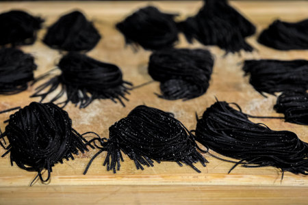 Fresh squid ink homemade spaghetti pasta nests, sprinkled with semolina flour drying on a wooden cutting boardの写真素材