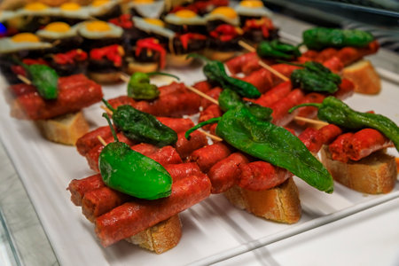 Traditional Spanish pintxos or tapas of pork sausages with green peppers on display in a restaurant,...