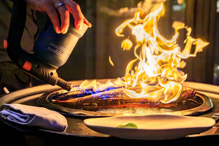 Branzino or Mediterranean sea bass seared with a torch fire at the table by a waiter at a street restaurant in Nice, French Riviera, South of Franceの写真素材