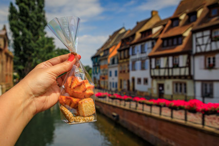 Woman s hand holding a bag of artisanal cookies with half timbered houses above channels of the River Lauch in Petite Venise, Colmar, Alsace, Franceの写真素材